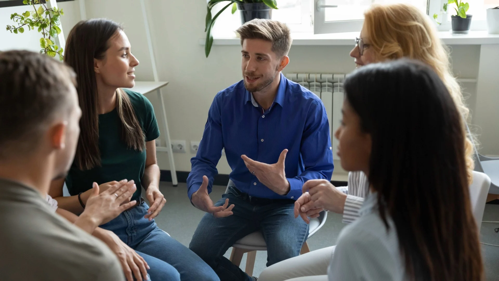 A man in a dark blue shirt sits and speaks surrounded by his colleagues.